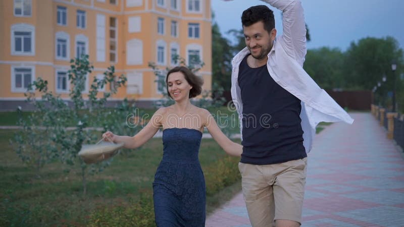 Caminhada feliz do divertimento dos recém-casados dos pares ao longo do passeio perto de sua casa nova