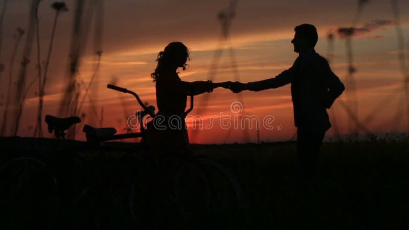 Caminhada romântica dos pares na dança do amor no campo durante o por do sol vermelho brilhante Vista das silhuetas