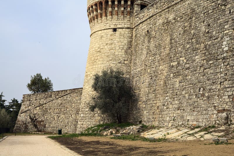 Caminho de cascalho próximo a uma torre e um muro de fronteira com uma oliveira ao seu lado num parque num dia nublado