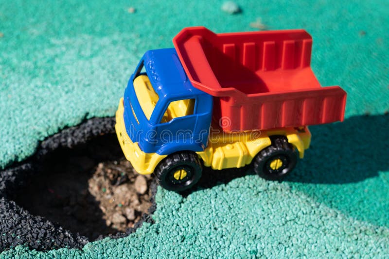 Camion di plastica del giocattolo con un corpo rosso fermato davanti al pozzo L'automobile non può andare Foro su asfalto La str fotografie stock libere da diritti Camion di plastica del giocattolo con un corpo rosso fermato davanti al pozzo L'automobile non può andare Foro su asfalto La str fotografie stock libere da diritti