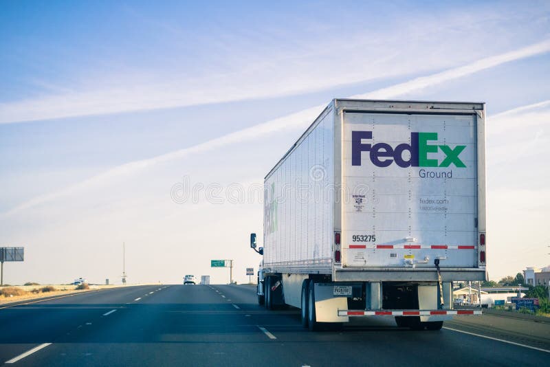 Camión del FedEx Ground que conduce en la autopista sin peaje en un soleado el domingo por la mañana imágenes de archivo libres de regalías Camión del FedEx Ground que conduce en la autopista sin peaje en un soleado el domingo por la mañana imágenes de archivo libres de regalías