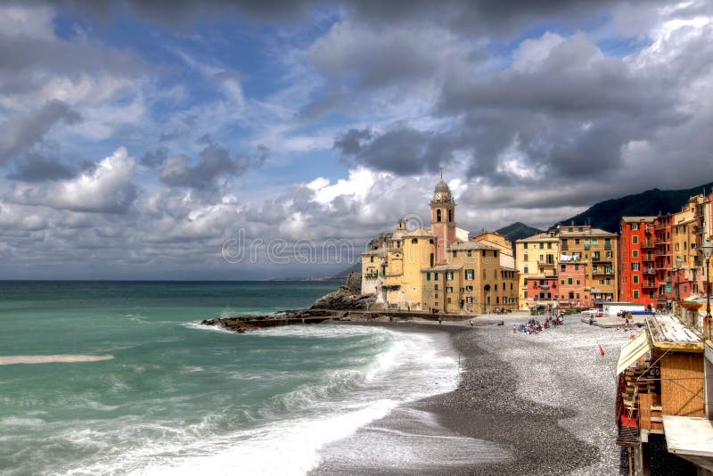 Camogli is a small fishing town and summer resort on Ligurian coast near Genoa, Italy. Its attractive seafront promenade ends with a small harbour under the protection of both of a church and castle (Basilica di Santa Maria Assunta and Castello della Dragonara). Dramatic cloudscape looming over the bright colored houses in late spring. HDR image. Camogli is a small fishing town and summer resort on Ligurian coast near Genoa, Italy. Its attractive seafront promenade ends with a small harbour under the protection of both of a church and castle (Basilica di Santa Maria Assunta and Castello della Dragonara). Dramatic cloudscape looming over the bright colored houses in late spring. HDR image.