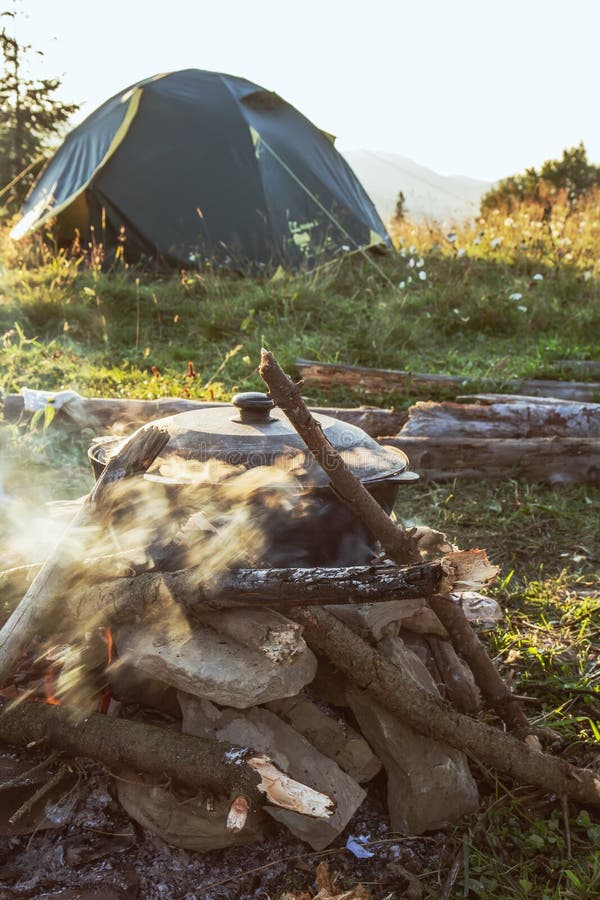 Camp de touristes avec le feu, le pot, la tente et le bois de chauffage images stock Camp de touristes avec le feu, le pot, la tente et le bois de chauffage images stock