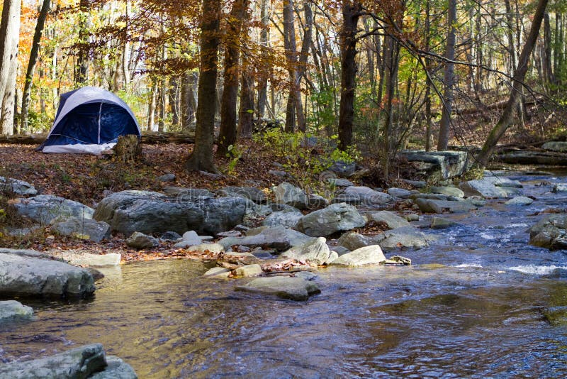 Small camping tent is pitched by a mountain stream in the woods in autumn with fall foliage. Small camping tent is pitched by a mountain stream in the woods in autumn with fall foliage.