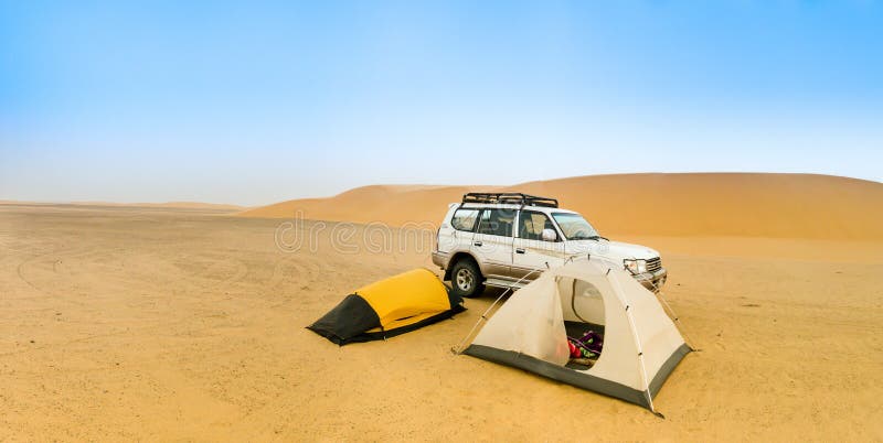 Camping in the Sudanese desert with two small tents, an off-road vehicle and a sand dune in the background