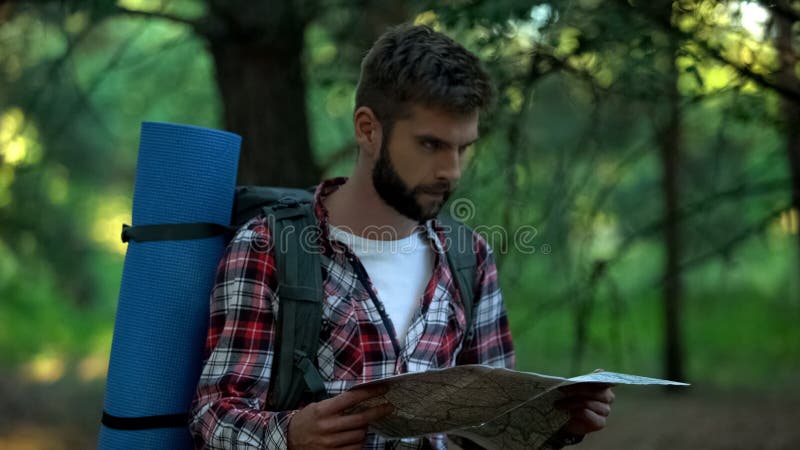 Campista confuso que orienteering com o mapa na floresta, procurando pela maneira direita foto de stock Campista confuso que orienteering com o mapa na floresta, procurando pela maneira direita foto de stock