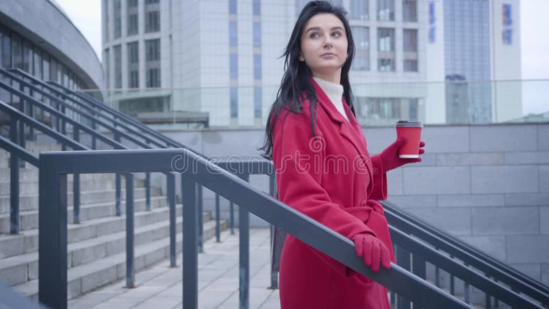 Caméra suivant la jeune jolie femme du caucase en descendant les escaliers dans la ville avec une tasse de café. Vue de côté de da