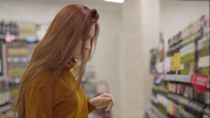 Caméra suivant la jeune jolie femme rousse activant la boisson au supermarché. Belle sélection concentrée de fille