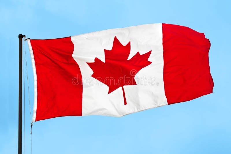 Kanadský vlajkou máva vo vetre na modrej oblohe.