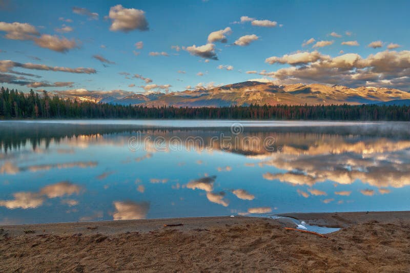 Morning sunrise in the Rocky Mountains on the beach of Annette Lake in Jasper National Park with reflections of Majestic Mountain and Aquila Mountain on the calm waters. Morning sunrise in the Rocky Mountains on the beach of Annette Lake in Jasper National Park with reflections of Majestic Mountain and Aquila Mountain on the calm waters