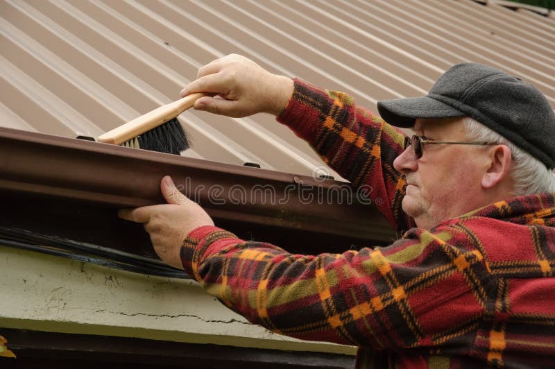 Senior male cleaning out the shed gutter with brush. Senior male cleaning out the shed gutter with brush