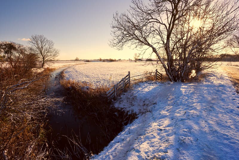 Canal and wooden fence in snow at sunrise
