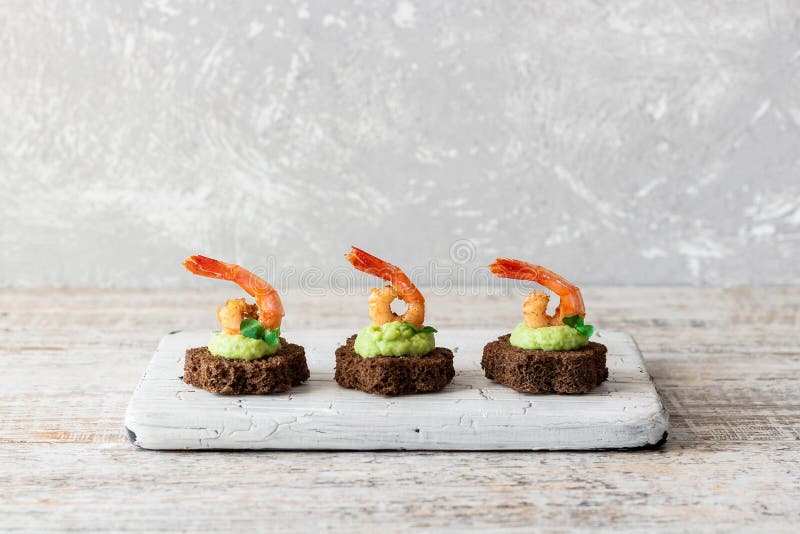 Canapes with avocado muslim and garlic shrimp on brown bread. Simple and easy snack for parties and banquets. Comfortable food. Canapes with avocado muslim and garlic shrimp on brown bread. Simple and easy snack for parties and banquets. Comfortable food