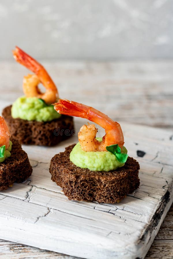 Canapes with avocado muslim and garlic shrimp on brown bread. Simple and easy snack for parties and banquets. Comfortable food. Canapes with avocado muslim and garlic shrimp on brown bread. Simple and easy snack for parties and banquets. Comfortable food