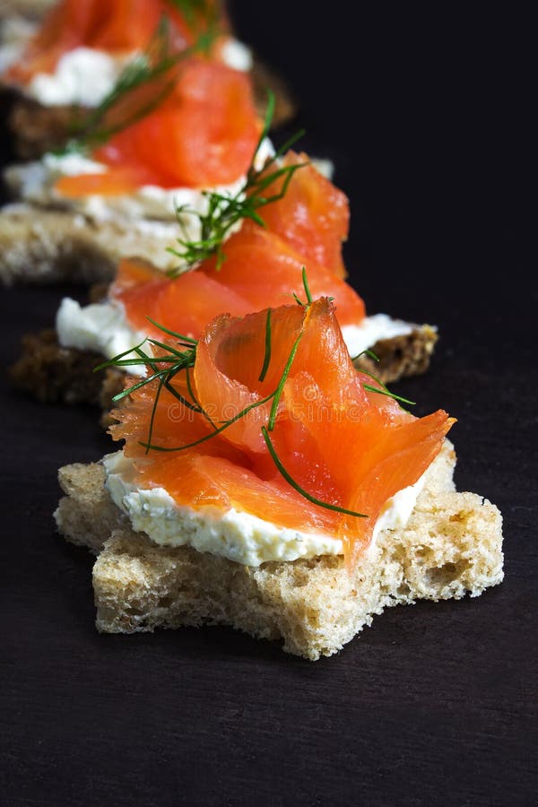 Canapes in star shape with smoked salmon on dark brown wood, fo