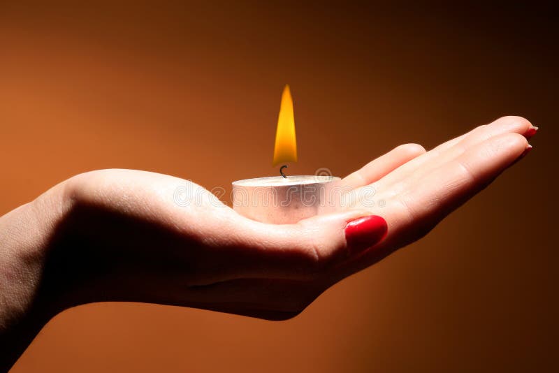 A burning candle in female hand on orange. A burning candle in female hand on orange