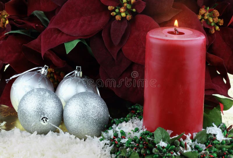 Burning Christmas candle surrounded by rich burgundy colored Poinsettias, silver ornaments and snow. Burning Christmas candle surrounded by rich burgundy colored Poinsettias, silver ornaments and snow.