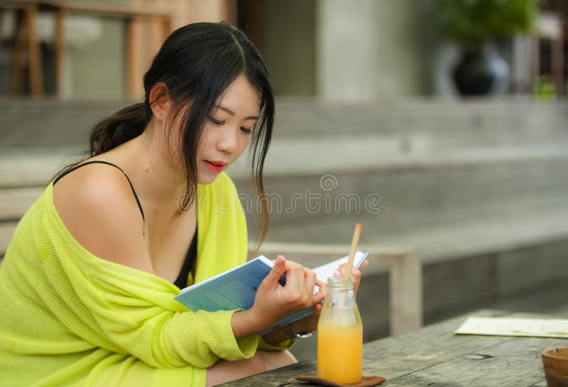 Candid lifestyle portrait of young beautiful and relaxed Asian Korean student girl on reading book or studying outdoors at coffee stock image Candid lifestyle portrait of young beautiful and relaxed Asian Korean student girl on reading book or studying outdoors at coffee stock image