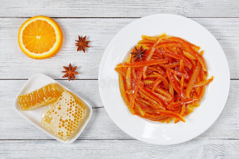 Delicious sweet Homemade candied orange and lemon peels on white plate on wooden table with Honey and half of orange on background, view from above. Delicious sweet Homemade candied orange and lemon peels on white plate on wooden table with Honey and half of orange on background, view from above