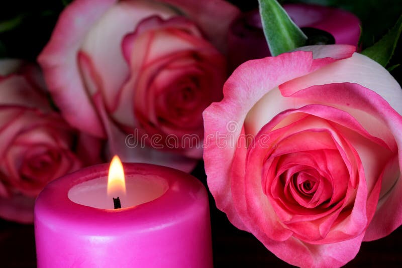 A candle is burning next to white-red roses