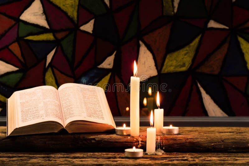 Bible crucifix and beads with a candle on a old oak wooden table. Beautiful Stained-glass windows background.Religion concept.