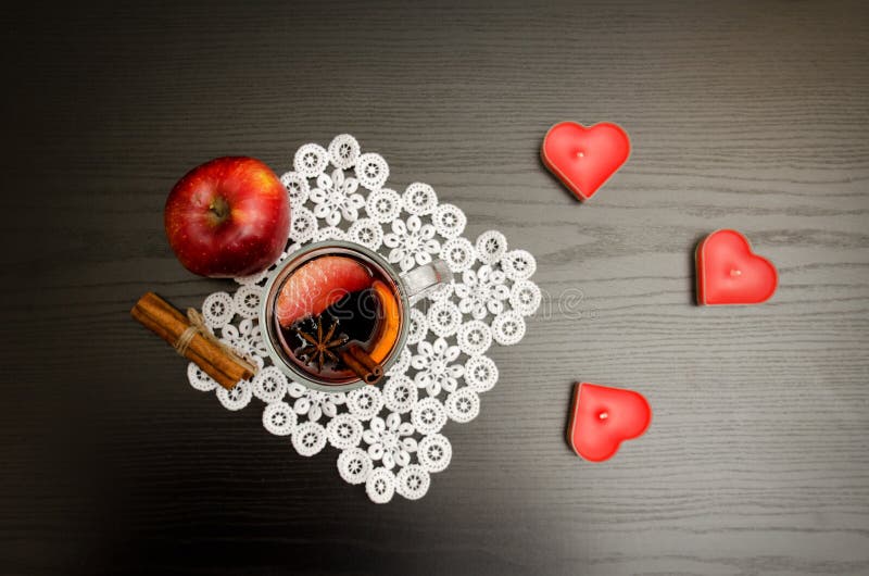 Candles in the shape of a heart, mulled wine with spices on a lace napkin, apple and cinnamon sticks. Black wood background stock photos Candles in the shape of a heart, mulled wine with spices on a lace napkin, apple and cinnamon sticks. Black wood background stock photos