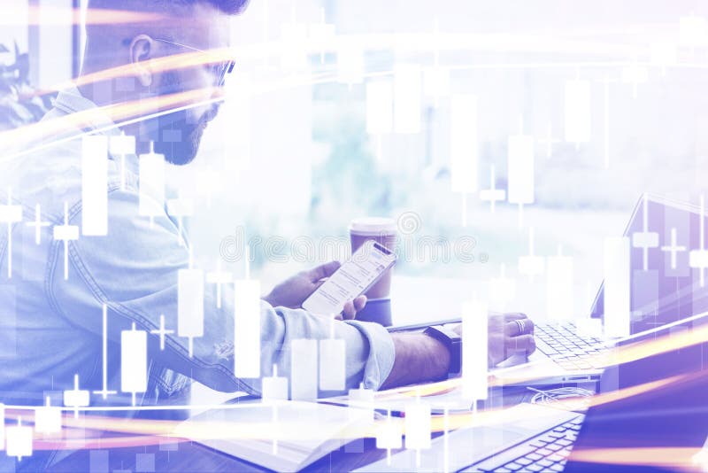 Candlestick chart in foreground. In background man sits, uses smartphone, works on laptop. Businessman reads message in phone stock photo