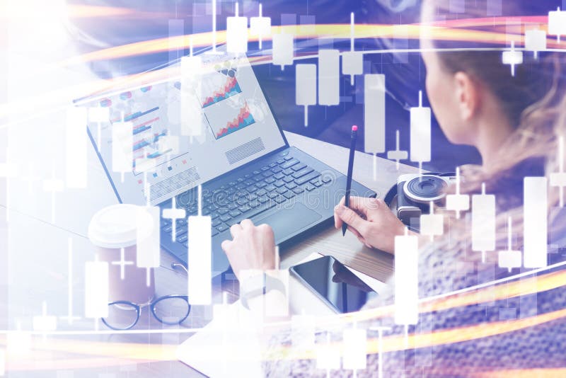 Candlestick chart in foreground. In background woman working on laptop computer with graphs, charts, diagrams on monitor stock photography