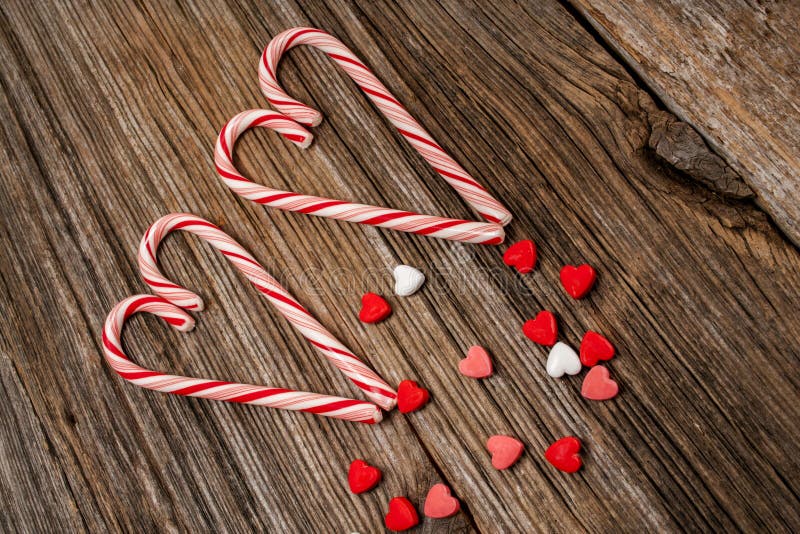 Two candy canes in shape of heart with candy hearts on old barnwood boards. Two candy canes in shape of heart with candy hearts on old barnwood boards