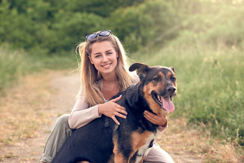 Cane nero sorridente felice che indossa un cablaggio di camminata che si siede affrontando il suo proprietario grazioso della gio immagini stock libere da diritti