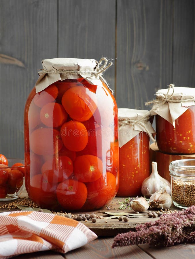 Canned tomatoes in glass jar on wooden rustic table in pantry or village kitchen, closeup