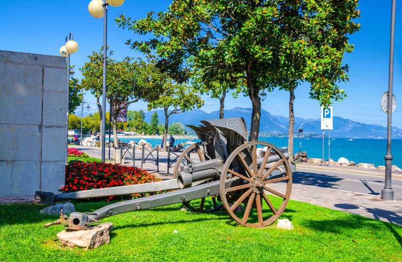 Cannon on green grass lawn in historical centre of Desenzano del Garda town. With view of Garda Lake promenade embankment and mountain range, blue sky stock photos Cannon on green grass lawn in historical centre of Desenzano del Garda town. With view of Garda Lake promenade embankment and mountain range, blue sky stock photos