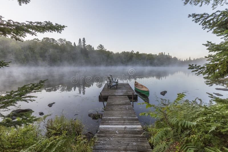 Canoa y muelle verdes en una mañana brumosa - Ontario, Canadá foto de archivo Canoa y muelle verdes en una mañana brumosa - Ontario, Canadá foto de archivo