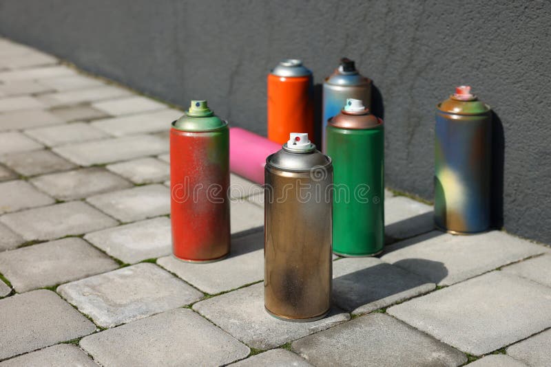 Cans of Different Spray Paints on Pavement Near Wall Stock Photo