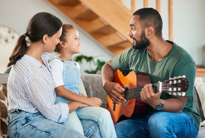 Cantando una canción especial para sus damas especiales. un padre tocando una guitarra acústica para su esposa y su hija pequeña e