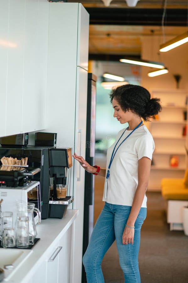 Young Darkhaired Woman in the Office Making Coffee in the Office
