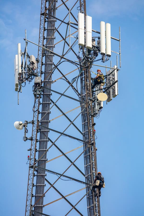 Canton, Ohio lake, USA. May 8, 2019. Communication maintenance. Two technicians climbing on telecom tower antenna against blue sky background. Canton, Ohio lake, USA. May 8, 2019. Communication maintenance. Two technicians climbing on telecom tower antenna against blue sky background