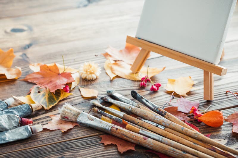 Canvas on easel, paint tubes, brushes and autumn leaves on desk.