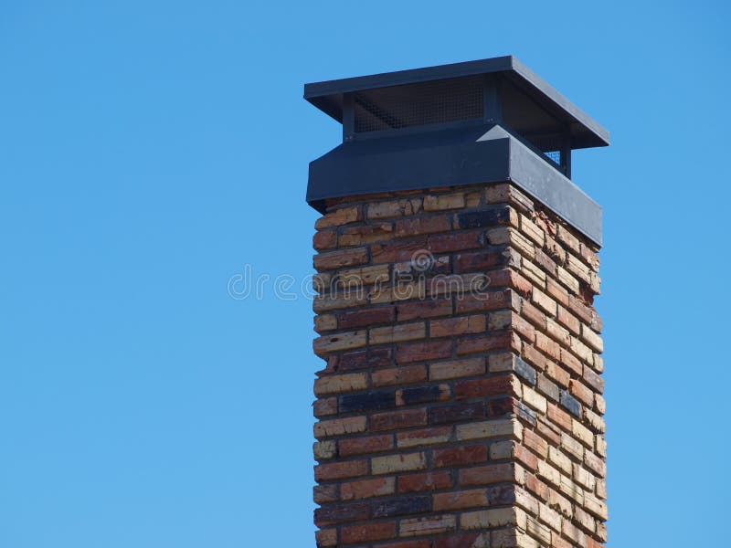 A Brick Chimney on a Blue Sky with a Sturdy Cap