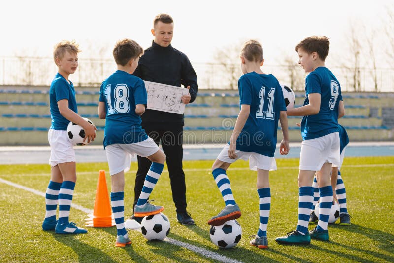 Capacitación en tácticas de fútbol para niños. chicos con entrenador en el campo de fútbol. entrenador hablando del plan de juego imagenes de archivo