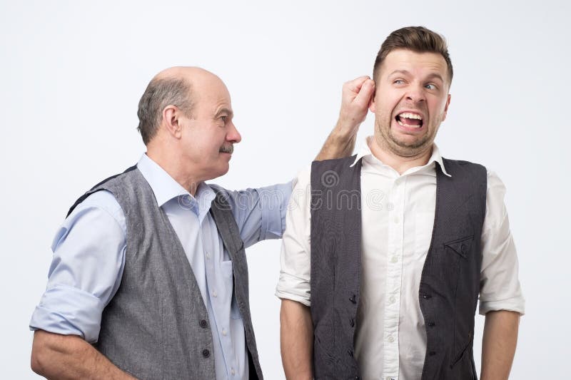 Capo senior che tira l'orecchio del giovane, punente per l'errore sul lavoro fotografie stock Capo senior che tira l'orecchio del giovane, punente per l'errore sul lavoro fotografie stock