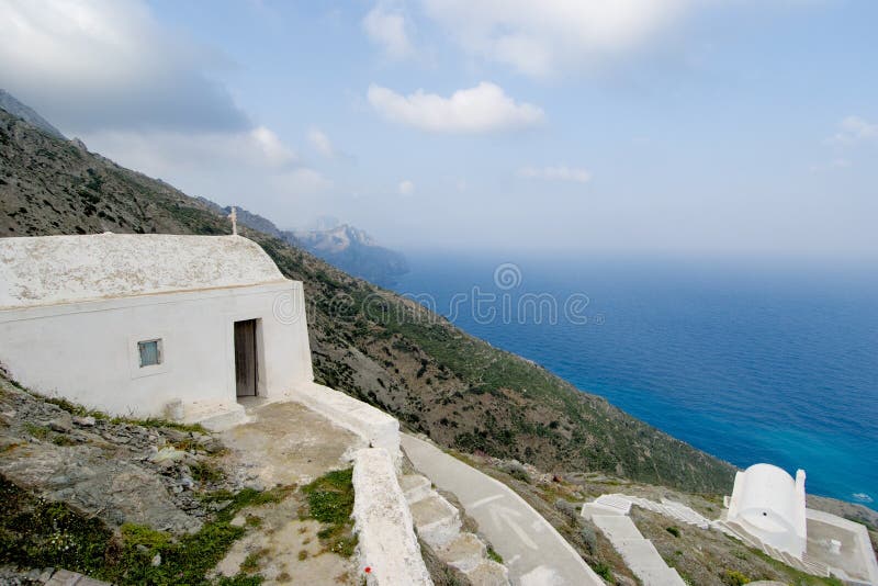 Cappelle bianche su una scogliera in Olympos, isola Grecia di Karpathos. Una cappella di due famiglie che appende sulla parete di una scogliera sul lato ovest del villaggio del villaggio di Olympos, isola di Karpathos, Grecia