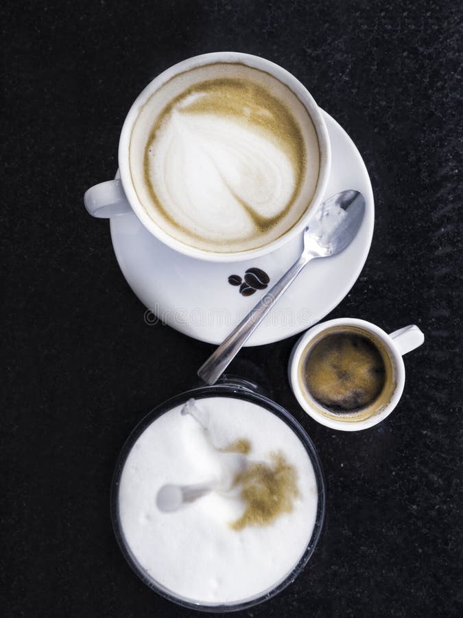 Cappuccino caldo, caffè nelle tazze bianche, latte del caffè espresso in vetro sulla tavola