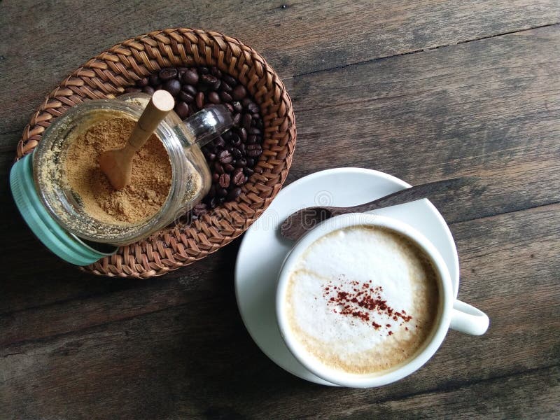 Cappuccino with coffee beans and sugar cane powder. Cappuccino with coffee beans and sugar cane powder in a basket on the old wooden desk as background stock images Cappuccino with coffee beans and sugar cane powder. Cappuccino with coffee beans and sugar cane powder in a basket on the old wooden desk as background stock images