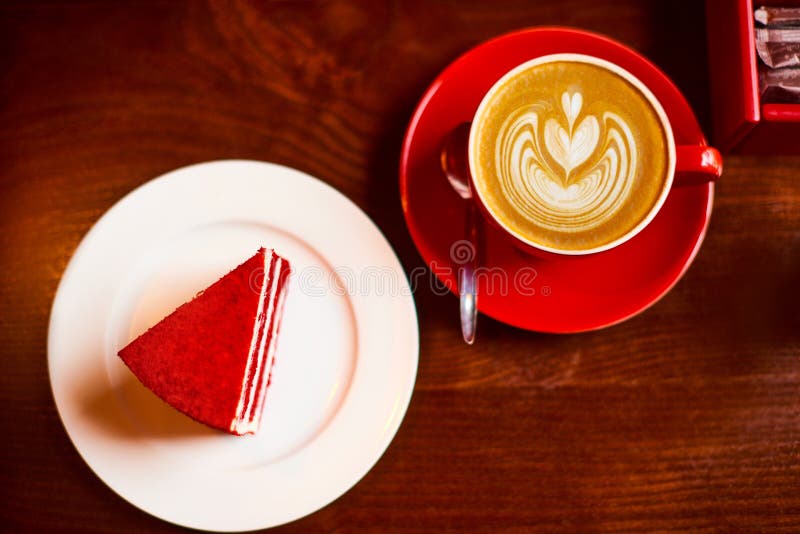 Cappuccino konstkaffe med hjärtdesign på toppen i röd kopp med röd sammetstårta på träbordet Kärlekskonfektyr royaltyfria bilder Cappuccino konstkaffe med hjärtdesign på toppen i röd kopp med röd sammetstårta på träbordet Kärlekskonfektyr royaltyfria bilder