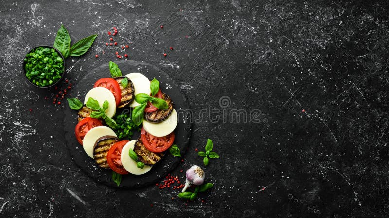 Caprese salad with basil. Tomatoes, mozzarella cheese and eggplant on a black stone plate. Top view. Free space for your text