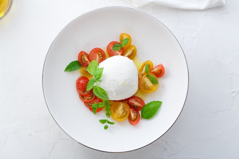 Caprese salad with red and yellow tomatoes, mozarella, basil and olive oil. Close view. White background top view