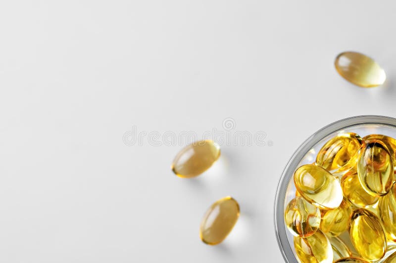 Capsules of fish oil omega-3 in a glass bowl and on a white stschl nearby. Flat lay with copy space, white background