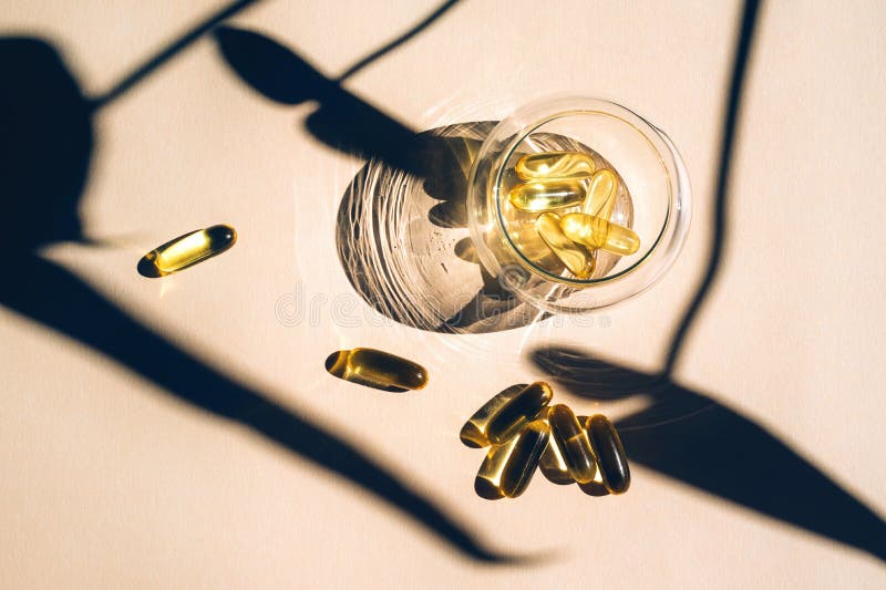 Capsules fish oil omega-3 in glass cup with a shadow of monstera leaves in the sunlight on the beige background.