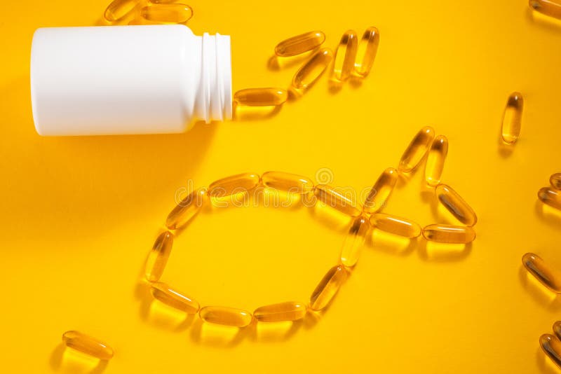Capsules spilled out of white bottle and made shape of fish on orange background